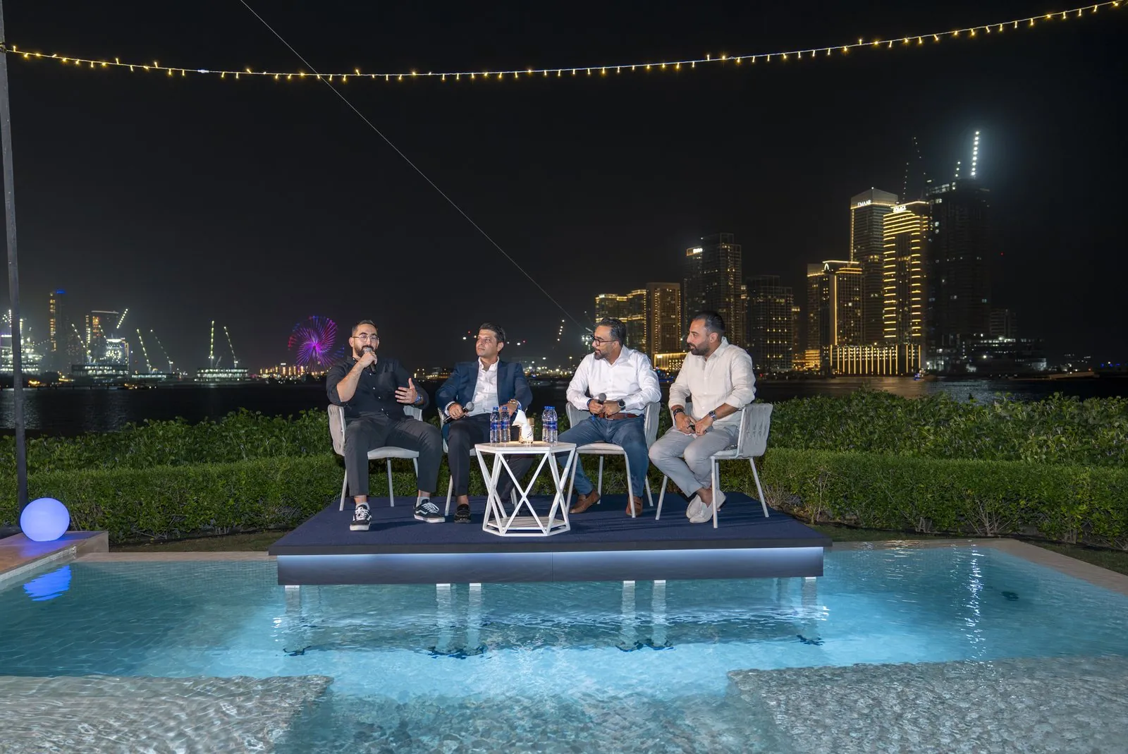 Four-person panel discussion on a pool stage at night